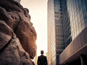 man standing between a large rock and a skyscraper